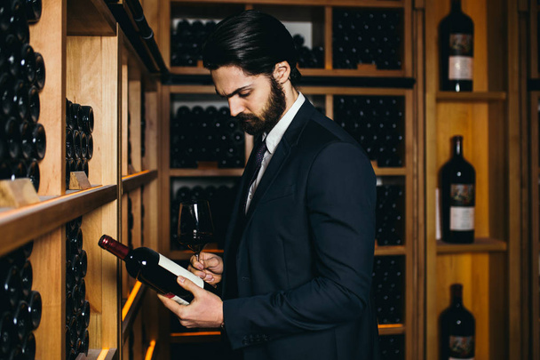 Young sommelier choosing a bottle of wine at the wine cellar.  - Zdjęcie, obraz