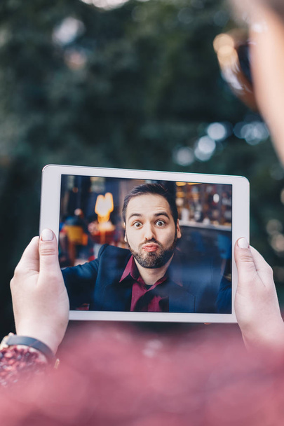 Young woman using a tablet, having a video call chat with her businessman boyfriend who is sending her kisses while he's away on a business trip. Concept of keeping long distant relationship. - Photo, Image