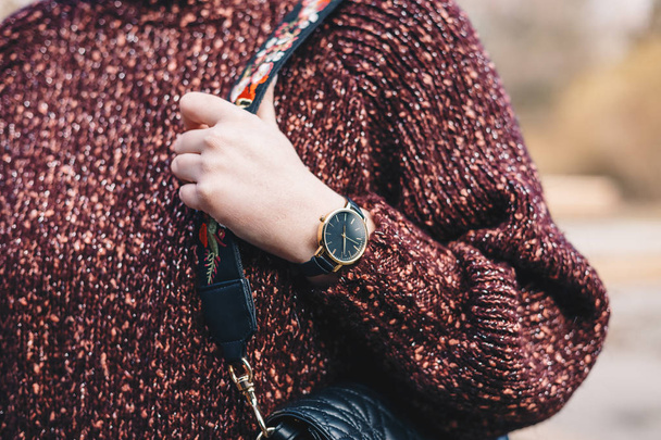 Γκρο πλαν του κορμού της νεαρής γυναίκας σε κόκκινο πουλόβερ, φοράει το ρολόι χειρός και ένα μαύρο καπιτονέ τσαντάκι. Εικόνα κατακόρυφη. - Φωτογραφία, εικόνα