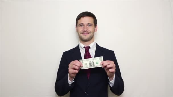 Young handsome businessman shows one dollar and verifies its authenticity by stretching to the sides.Portrait on white background - Materiał filmowy, wideo