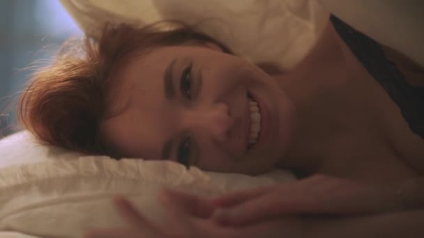 Szép nő, csodálatos mosolyt keres, a kamera az ágyban fekve közelről. Lövés a takaró alatt - Felvétel, videó