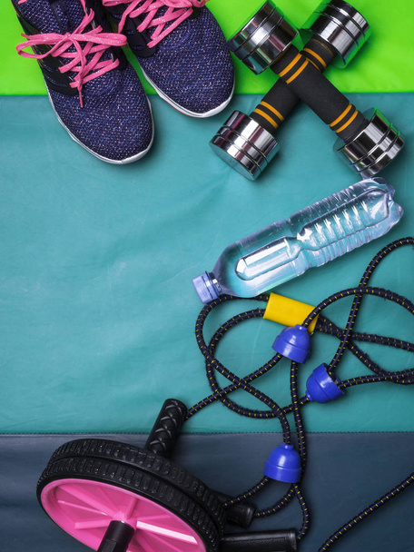 Accessoires de sport vue de dessus. Baskets femme, bouteille d'eau, extenseur, presse rouleau sur tapis vert, espace de copie
 - Photo, image