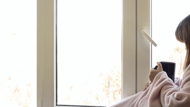 одна жінка в теплому рожевому халаті п'є гарячий чай з великої синьої чашки біля вікна
 - Кадри, відео