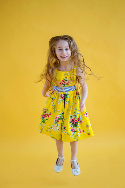 美しいドレスの色黄色の背景でジャンプ陽気なかわいい女の子 - 写真・画像