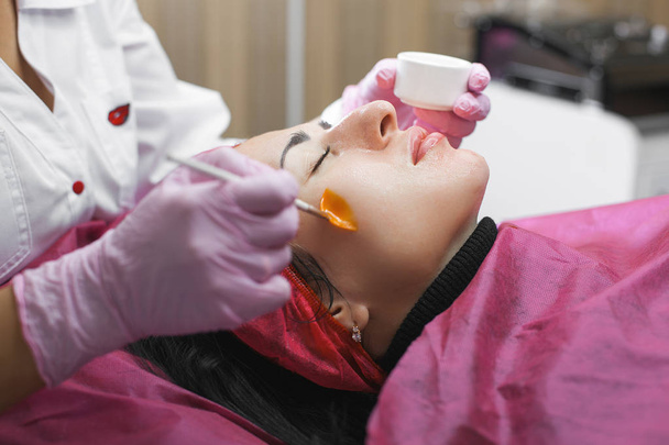 美容師は彼女の患者とフェイスマスクにフェイスマッサージを作ります。美容室でのアンチエイジング・スムーズな施術。皮膚ケアの治療を行う美容クリニックの医師 - 写真・画像