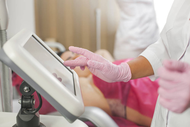 Doctor`s hands typing on the medical equipment. Unrecognizable medic. Close up still of hands wearing latex gloves. Cosmetologist doing the procedure of laser epilation - Photo, Image