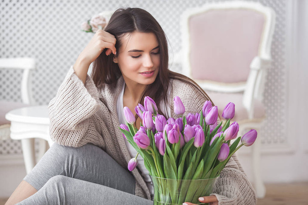 Nahaufnahme Porträt einer jungen schönen Frau im Haus. attraktive Frau mit Blumen. Weibchen mit Tulpen. Frühlingsstrauß. - Foto, Bild