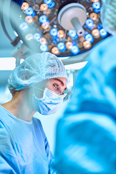 Close up portrait of young female surgeon doctor wearing protective mask and hat during the operation. Healthcare, medical education, surgery concept - Photo, image