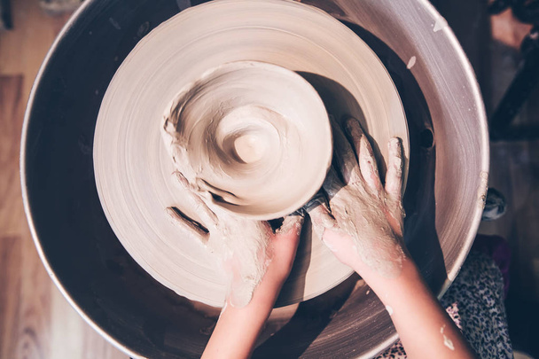 Vue du dessus de jeunes mains de potier formant un vase en céramique avec de l'argile sur la roue de poterie à l'atelier
 . - Photo, image
