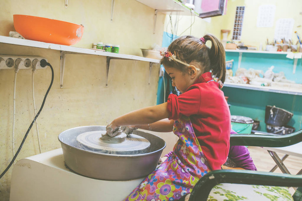 Mała dziewczynka kreatywne uczenie się w warsztacie garncarskim - Dziecko kształtowania gliny na kole ceramiki  - Zdjęcie, obraz