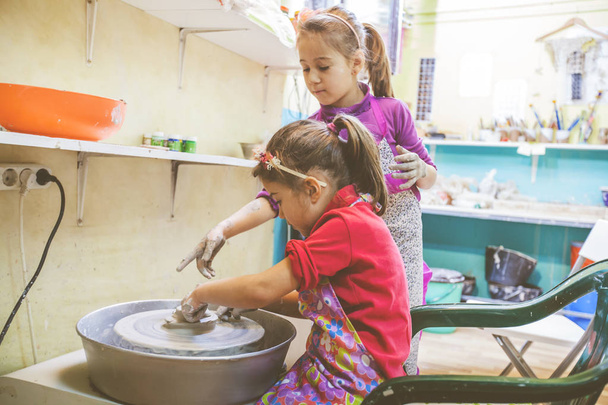 Dwie małe dziewczynki kreatywnej nauki na warsztatach garncarskich w studio sztuki - Dziecko kształtowania gliny na kole ceramiki  - Zdjęcie, obraz