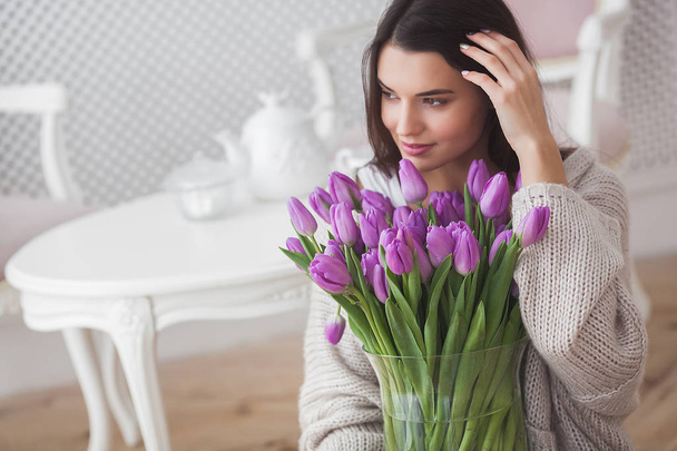 Aantrekkelijke jonge vrouw met bloemen binnen in de slaapkamer. Portret van mooie dame thuis. Close-up shot van vrouw met tulpen. - Foto, afbeelding