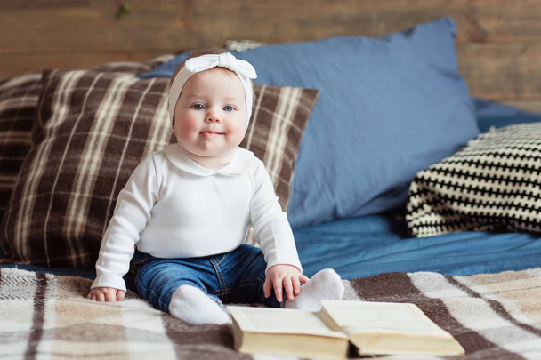 A young baby girl sits in a bad and reads a book. Happy childhood and earlier development concept - 写真・画像