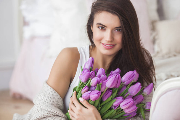 Portret van jonge mooie vrouw binnenshuis close-up. Aantrekkelijke vrouw met bloemen. Vrouw met tulpen. Lente boeket. - Foto, afbeelding