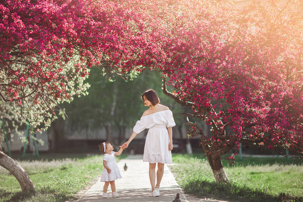 若い母親と彼女の小さな娘が、春に一緒に公園を散歩します。幸せな家族は屋外。愛らしい赤ちゃんの女の子を愛する. - 写真・画像