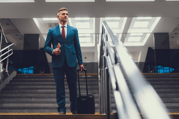 Handsome man with suitcase on stairs looking aside - Foto, imagen
