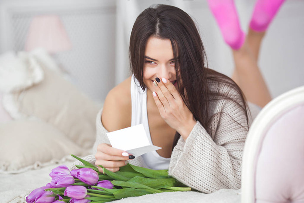 Young attractive woman with flowers reading a note from boyfriend. Lady indoors with flowers reading a message from lover. Valentine congrats. - Photo, Image