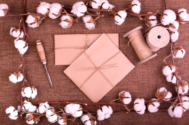 Flower design with fluffy dried cotton bolls and gift boxes over rough brown burlap. Top view, copy space, greeting card - Photo, Image