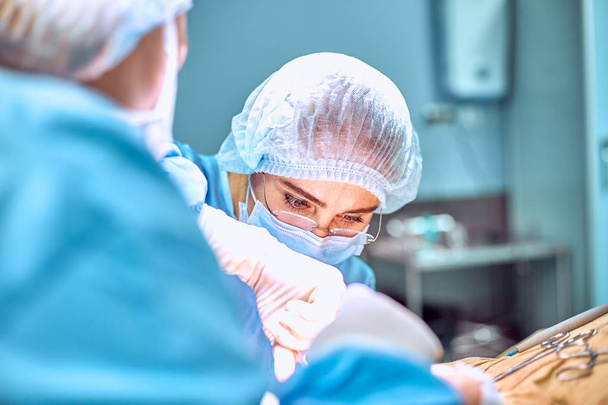 Close up portrait of young female surgeon doctor wearing protective mask and hat during the operation. Healthcare, medical education, surgery concept - Photo, Image