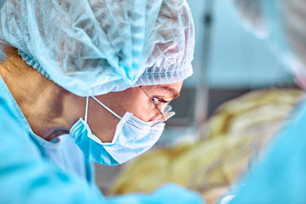 Bliska portret młoda kobieta chirurg lekarz maska ochronna i kapelusz na sobie podczas operacji. Opieka medyczna, edukacja, koncepcja operacji - Zdjęcie, obraz