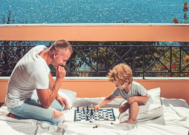father with son on balcony play chess. father and son have good time together. - Foto, afbeelding