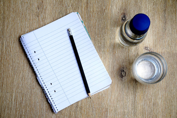 Caderno com papel forrado, lápis, copo de água e uma garrafa de vidro com água
 - Foto, Imagem