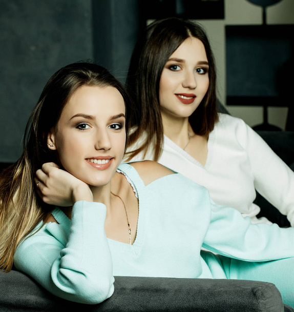 Two smiling friends sitting on the couch looking at camera in sitting room at home - Фото, изображение