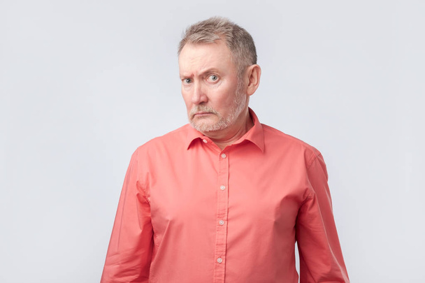 Senior férfi piros inget, komor és hunyorogva, bemutatva a hitetlenség, vagy kétséges - Fotó, kép