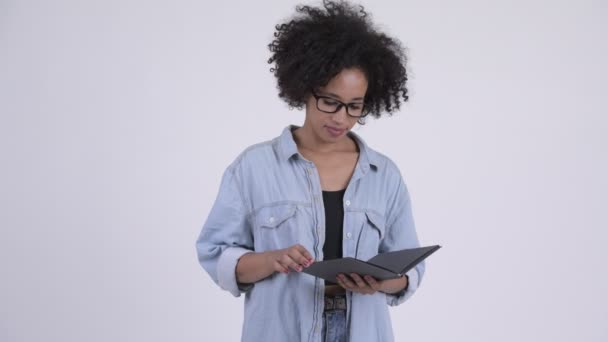 Young beautiful African woman with eyeglasses covering face with book - Imágenes, Vídeo