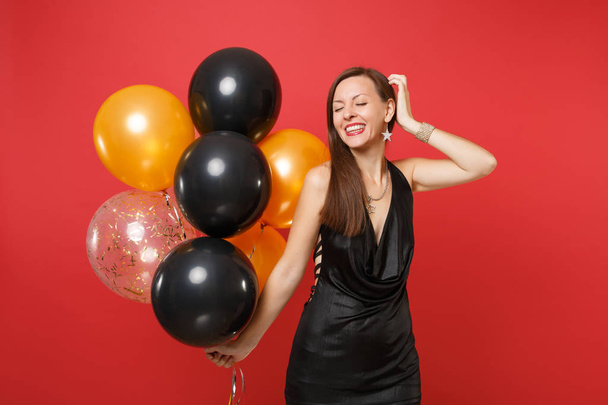 Atraktivní mladá žena v černých šatech slaví, položil ruku na hlavu drží s vrtulovým pohonem izolované na červeném pozadí. Mezinárodní Dámské den šťastný nový rok narozeniny maketa holiday party koncept. - Fotografie, Obrázek