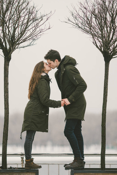 男は愛生と白人女性の異性カップル若い人。氷で覆われた冬を市の広場で、彼らは歩いて、抱擁し、キスします。どんな天候での愛の概念. - 写真・画像