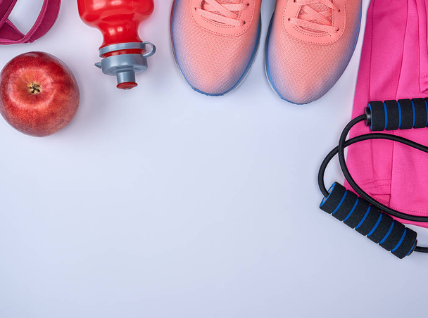 pink sports sneakers and a red water bottle, black jump rope on a white background, top view, copy space - 写真・画像