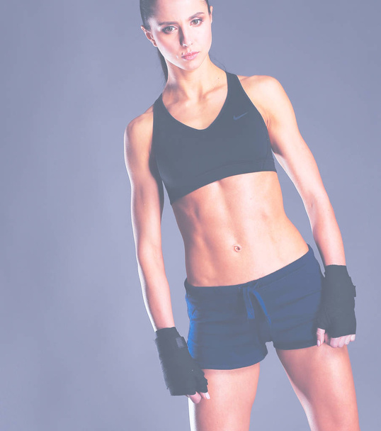 Muscular young woman posing in sportswear against black background. - Фото, изображение