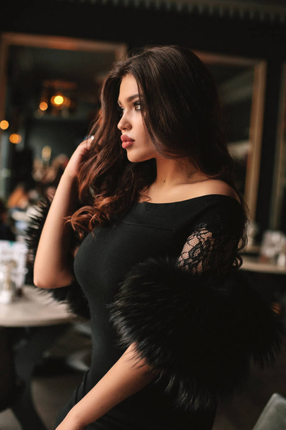 fashion photo of beautiful young woman with dark hair in elegant dress sitting in cafe - Photo, Image