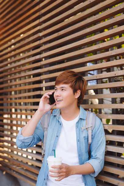 Joven asiático hombre sonriendo y hablando en el teléfono móvil fuera con espacio de copia a la izquierda
 - Foto, imagen