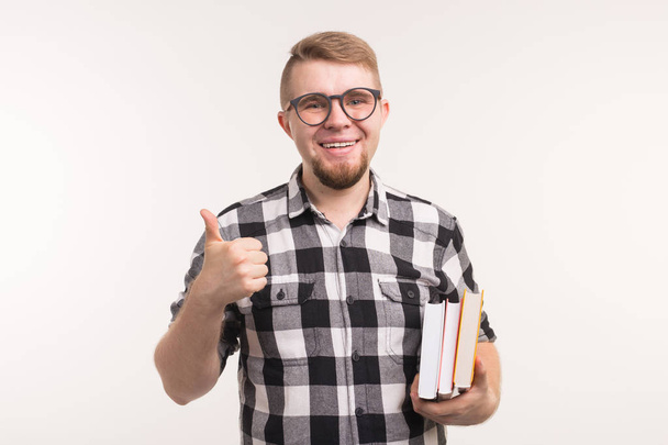 Concepto de personas y educación - Estudiante sonriente sosteniendo libros y haciendo gestos con los pulgares hacia arriba sobre fondo blanco
 - Foto, imagen