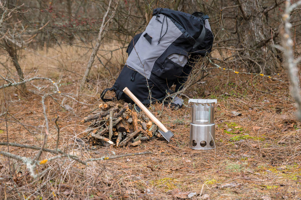 hacha cerca de una leña, estufa de leña de camping y backpactk en el fondo
 - Foto, imagen