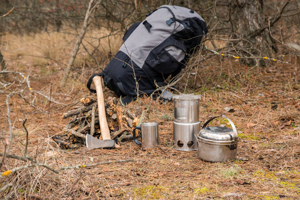 сокира біля дров, дерев'яна піч для кемпінгу, посуд для кемпінгу та рюкзак на фоні
 - Фото, зображення