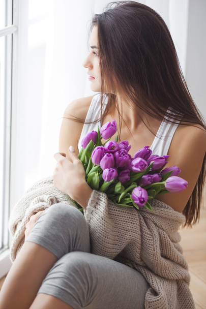 Mujer atractiva joven con ramo de flores. Hermosa chica en casa con tulipanes rosados. Mujer en el dormitorio
. - Foto, imagen
