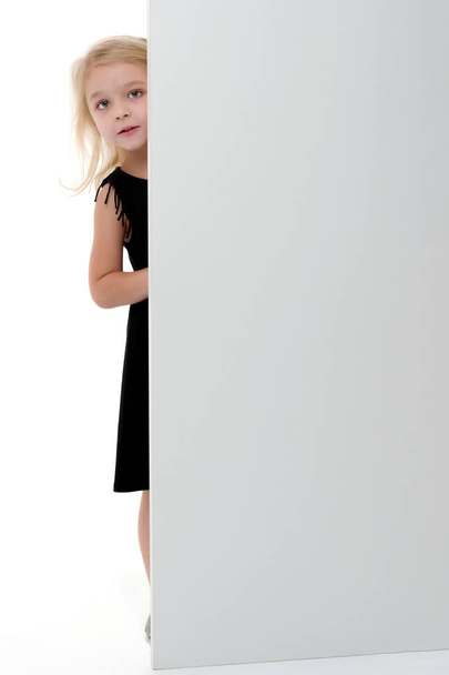A little girl is looking from behind an empty banner. - Foto, imagen