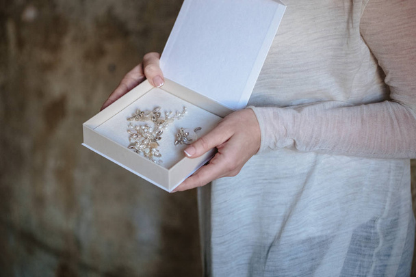 Woman's hands hold a white blank box with wedding handmade jewelry inside - 写真・画像