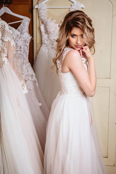 Hermosa novia rubia sentada cerca de armario vintage lleno de vestidos de novia. retrato de belleza de moda
  - Foto, Imagen