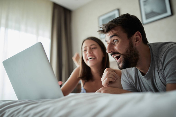 people, family, bedtime and fun concept -Young couple with laptop in bed surfing on the net at laptop - Photo, Image