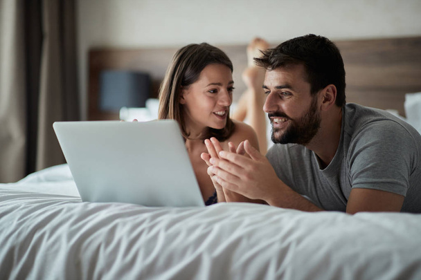 Smiling couple at home surfing the net in bed at morning - Foto, Bild