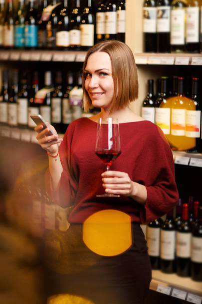 Photo of young blonde with glass in hands in store with wine - Foto, Imagen