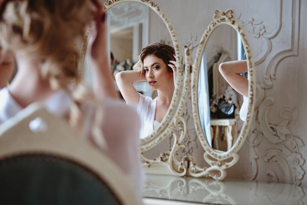 Portrait of blonde bride woman in a white lingerie sitting near mirror, fashion beauty portrait in interior  - 写真・画像