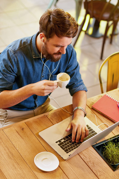 Male working at laptop and drinks coffee in cafe - Foto, Bild