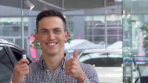 Happy male customer showing thumbs up holding car keys at the dealership - Photo, Image
