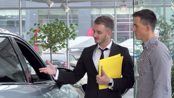 Дружелюбный автодебошир помогает своему клиенту-мужчине выбрать автомобиль для покупки
 - Фото, изображение