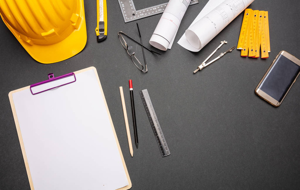 Architekt Ingenieur Arbeitsplatz, Baustellenschreibtisch. Projektbaupläne, gelber Hut und technische Hilfsmittel auf schwarz, Ansicht von oben - Foto, Bild